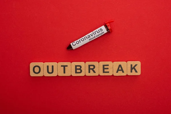 Top view of outbreak lettering on wooden cubes and test tube with blood sample on red background — Stock Photo