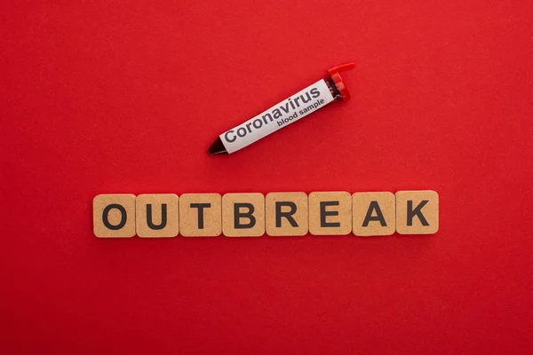 Vista dall'alto del lettering focolaio su cubi di legno e provetta con campione di sangue su fondo rosso — Foto stock