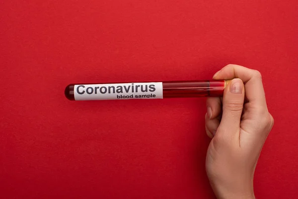 Top view of woman holding test tube with blood sample and coronavirus lettering on red background — Stock Photo