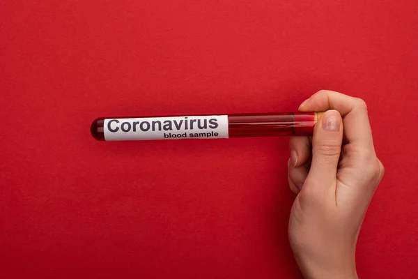 Vista superior de la mujer sosteniendo el tubo de ensayo con muestra de sangre y letras de coronavirus sobre fondo rojo - foto de stock