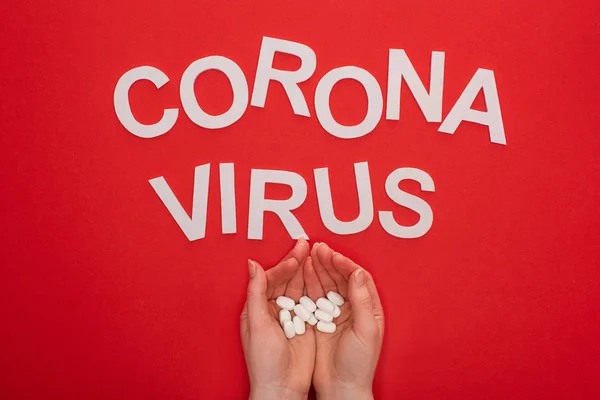 Top view of woman holding pills near coronavirus lettering on red background — Stock Photo