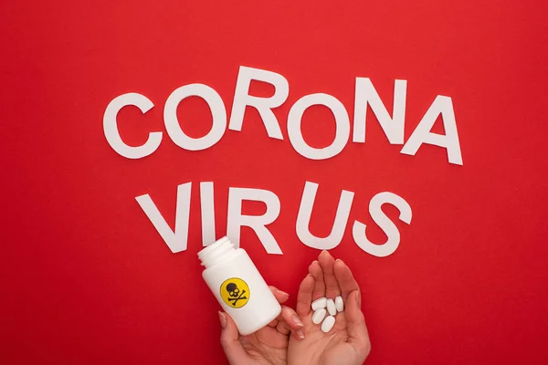 Top view of woman holding pills and jar with warning sign near coronavirus lettering on red background — Stock Photo