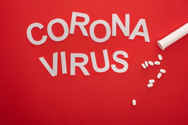 Top view of coronavirus lettering and pills on red background — Stock Photo