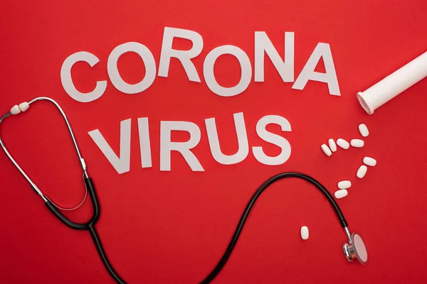 Вид зверху на стетоскоп і таблетки з коронавірусними плямами на червоному тлі — стокове фото