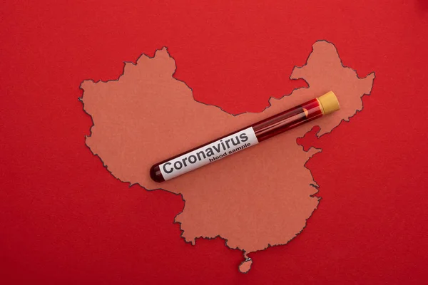 Top view of test tube with blood sample on wooden china map isolated on red — Stock Photo