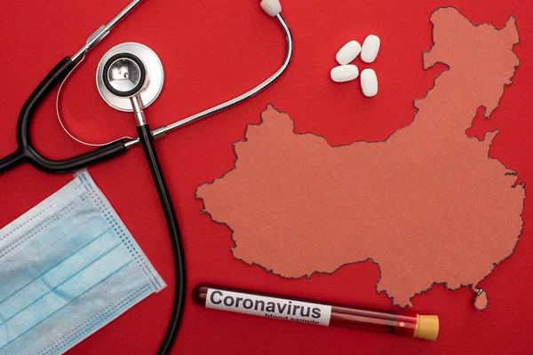 Вид сверху стетоскопа, медицинской маски и пробирки с коронавирусом рядом с картой Китая на красном фоне — Stock Photo