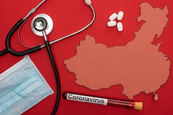 Top view of stethoscope, medical mask and test tube with coronavirus lettering near map of china on red background — Stock Photo