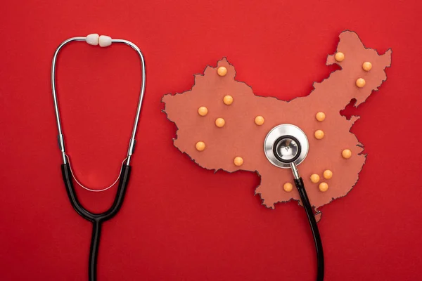 Vue du dessus de la carte de la Chine avec broches poussoirs et stéthoscope sur fond rouge — Photo de stock