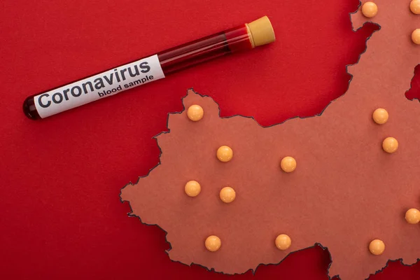 Draufsicht auf die Karte von China mit Stecknadeln und Reagenzglas mit Blutprobe und Coronavirus Schriftzug auf rotem Hintergrund — Stockfoto