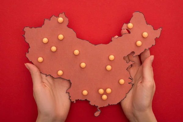 Top view of woman holding layout of china map with push pins on red background — Stock Photo
