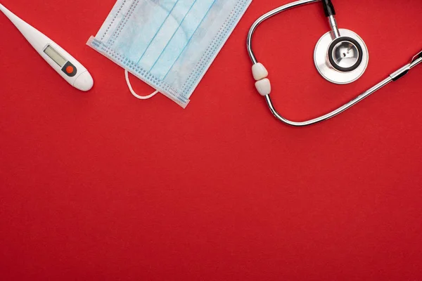Vista dall'alto della maschera medica con termometro e stetoscopio su sfondo rosso — Foto stock