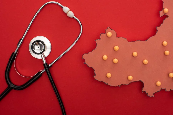 Top view of stethoscope and layout of china map with push pins on red background — Stock Photo