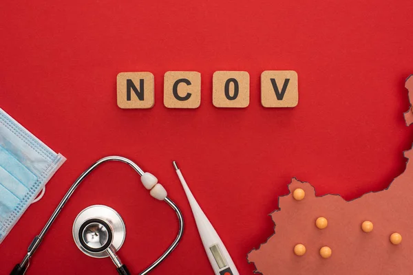 Top view of wooden cubes with ncov letters, medical mask with stethoscope and layout of china map on red surface — Stock Photo