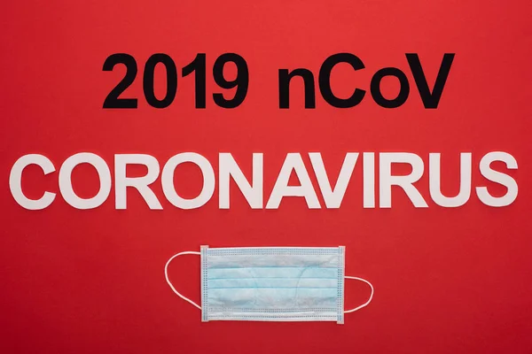 Vue du dessus du masque médical avec lettrage 2019 ncov et coronavirus isolé sur rouge — Photo de stock