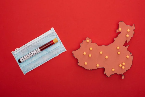 Visão superior do layout do mapa da China com letras coronavírus no tubo de teste e máscara médica no fundo vermelho — Fotografia de Stock