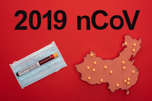 Top view of 2019 ncov lettering, layout of china map with test tube on medical mask on red surface — Stock Photo