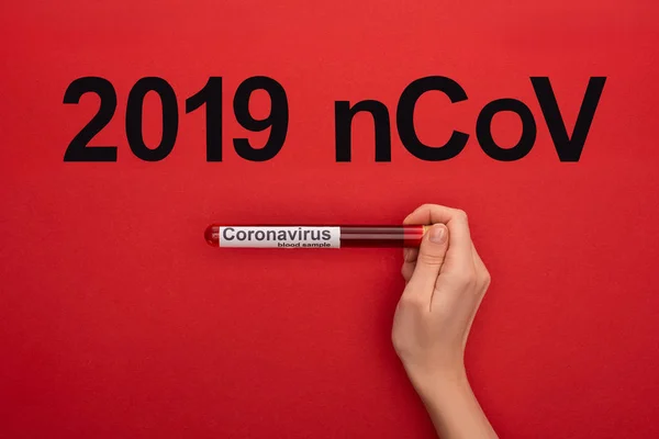 Top view of woman holding test tube with blood sample and 2019 ncov lettering on red surface, panoramic shot — Stock Photo