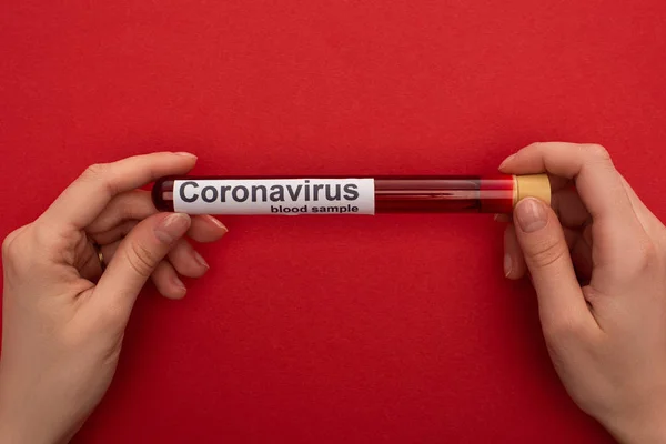 Top view of woman holding test tube with blood sample and coronavirus lettering on red surface — Stock Photo