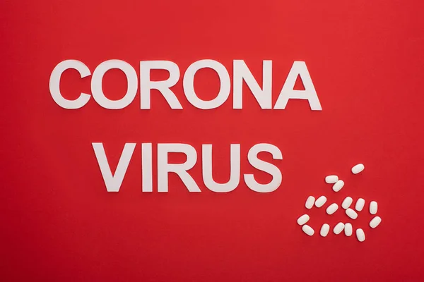 Vista dall'alto dell'iscrizione coronavirus con pillole sulla superficie rossa — Foto stock