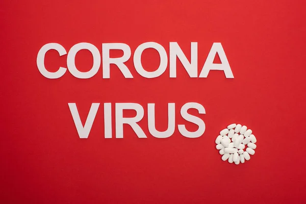 Top view of pills and coronavirus lettering on red background — Stock Photo