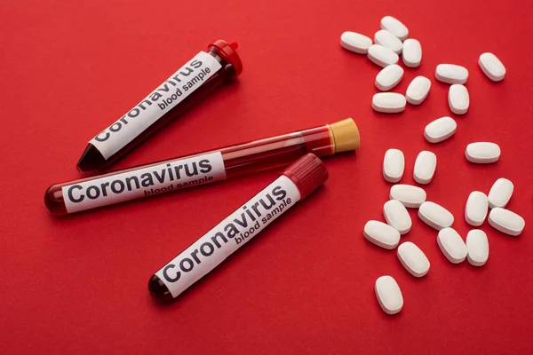 Close up view of pills and test tubes with blood samples and coronavirus lettering on red background — Stock Photo