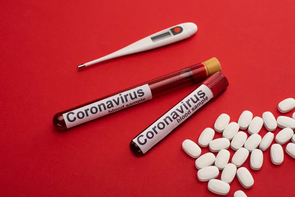 Pills, thermometer and test tubes with blood samples and coronavirus lettering on red surface — Stock Photo