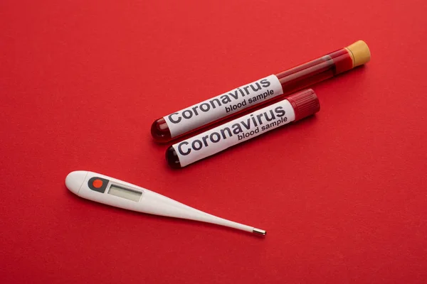 Close up view of thermometer, test tubes with blood samples and coronavirus lettering on red background — Stock Photo