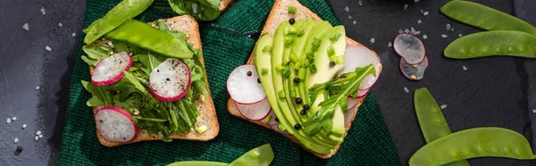 Panoramic shot of vegetarian sandwiches with radish, green peas and avocado on cloth — Stock Photo