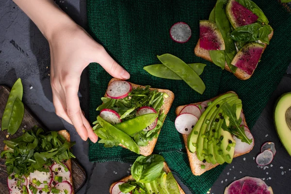 Vista recortada de la mujer tomando sándwiches con rábano, guisantes verdes y aguacate - foto de stock