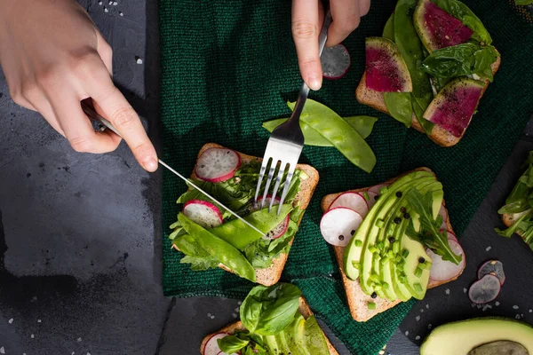 Cropped view of woman eating radish sandwiches with fork and knife — Stock Photo