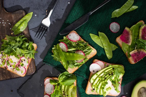 Vista dall'alto di panini vegetariani con verdure fresche su stoffa e taglieri con forchetta e coltello — Foto stock