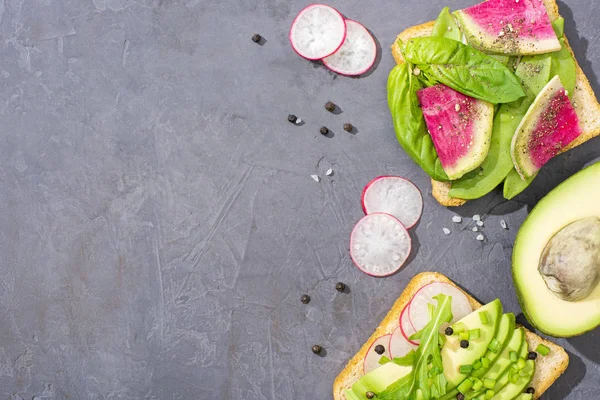 Top view of organic vegetarian toasts with fresh vegetables on table with pepper seeds and salt — Stock Photo