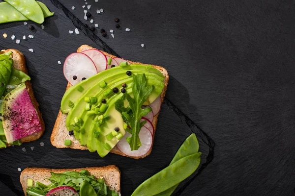 Top view of organic sandwiches with radish and avocado on stone board with pepper and salt — Stock Photo
