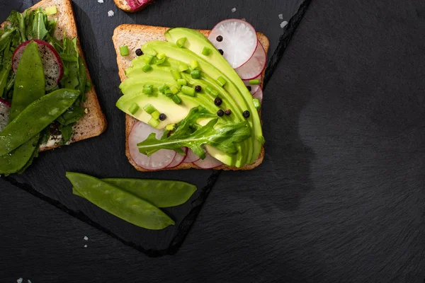 Top view of fresh sandwiches with radish and avocado on stone board with pepper and salt — Stock Photo