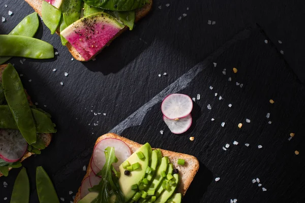 Top view of organic sandwiches with vegetables on stone board with pepper and salt — Stock Photo