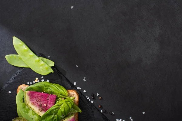 Top view of radish toast on stone cutting board with pepper seeds and salt — Stock Photo