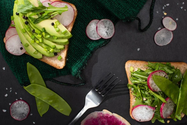 Vista superior de sándwiches vegetarianos saludables con rábano, guisantes verdes y aguacate sobre tela con tenedor - foto de stock