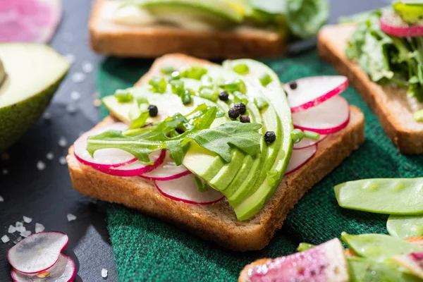 Свежие вегетарианские сэндвичи с редиской, авокадо и зеленым горошком на ткани — стоковое фото