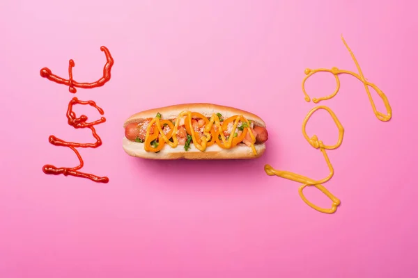 Vue du dessus de hot dog savoureux sur rose avec mot hot dog écrit avec ketchup et moutarde — Photo de stock
