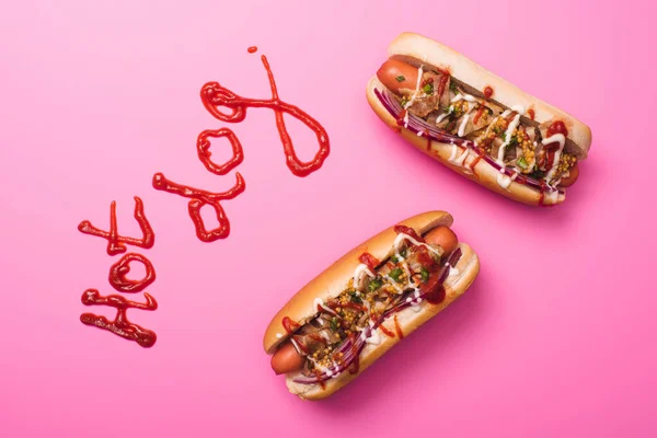 Vista superior de sabrosos hot dogs en rosa con palabra hot dog escrita con ketchup — Stock Photo