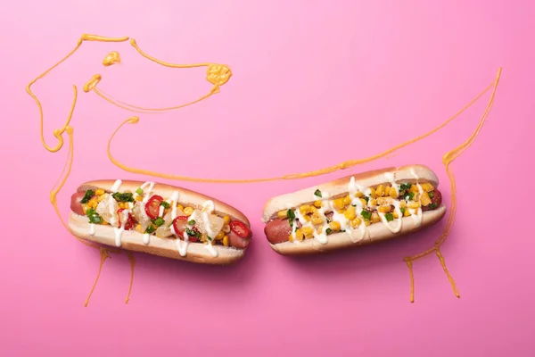 Вид сверху на два хот-дога на розовом с собакой, нарисованной горчицей — стоковое фото