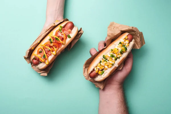 Cropped view of man and woman holding two tasty hot dogs in paper on blue — Stock Photo