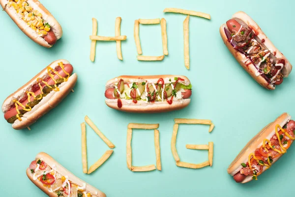 Vista superior de perritos calientes poco saludables en azul con palabra hot dog hecha de papas fritas - foto de stock