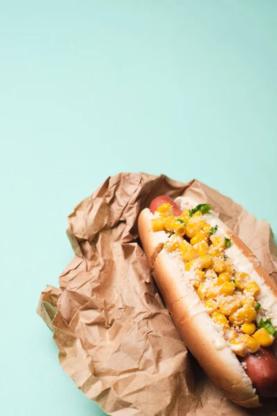 Delicious hot dog with corn in paper on blue — Stock Photo