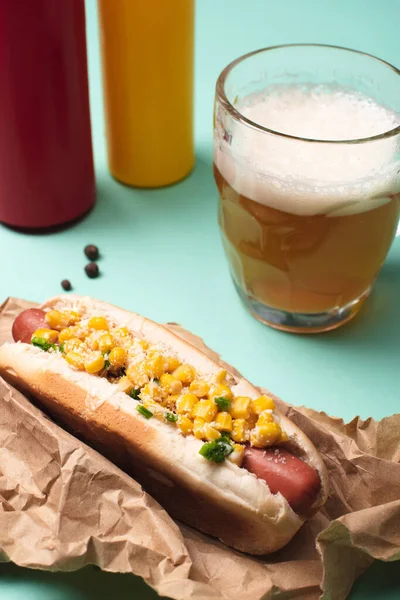 Gros plan de hot dog au maïs, verre de bière et bouteilles de moutarde et ketchup sur bleu — Photo de stock