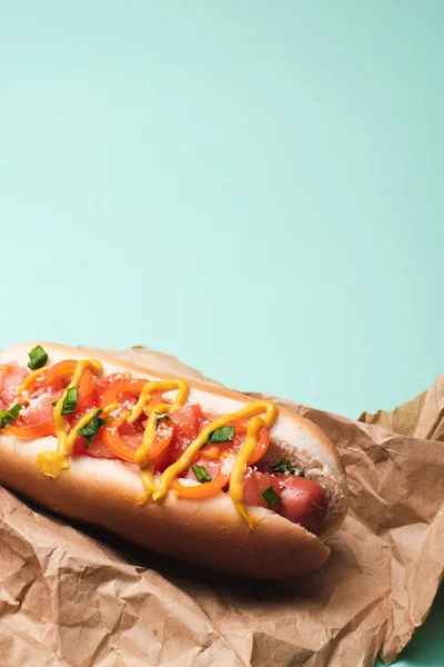 Hot dog délicieux à la moutarde en papier sur fond bleu — Stock Photo