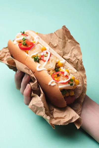 Vista ritagliata di donna che tiene gustoso hot dog in carta su blu — Foto stock
