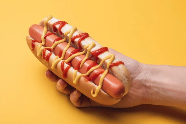 Cropped view of woman holding tasty hot dog on yellow — Stock Photo