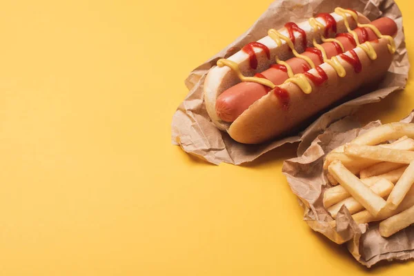 Köstliche Würstchen und Pommes in Papier auf gelb — Stockfoto