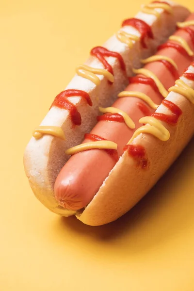 Primer plano de perrito caliente poco saludable con salchicha, mostaza y ketchup en amarillo - foto de stock